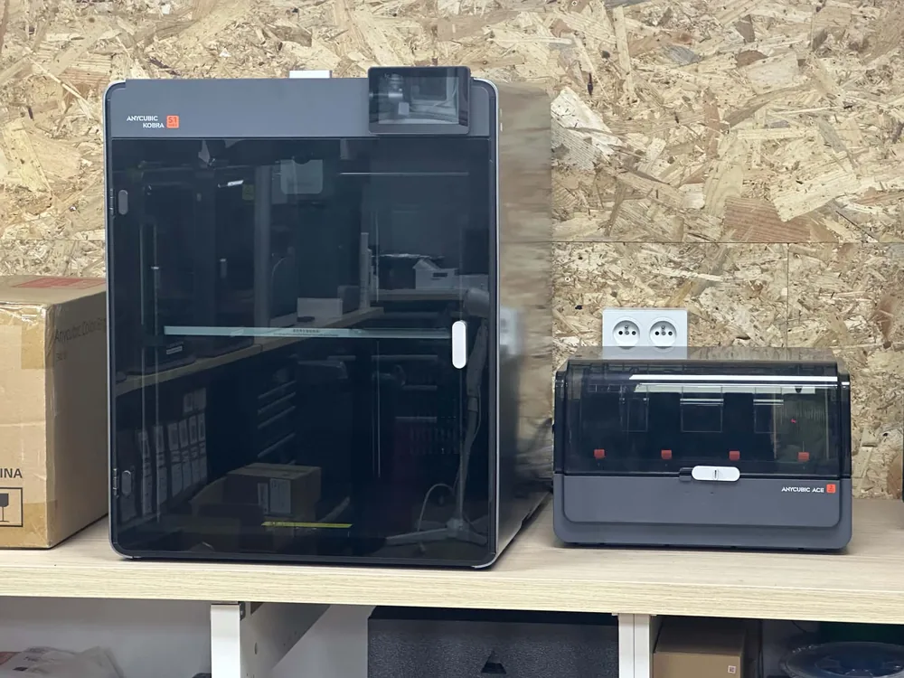 Imprimante Anycubic Kobra S1 Max et son chargeur ACE 2, posées sur une étagère de l'atelier devant un mur en OSB