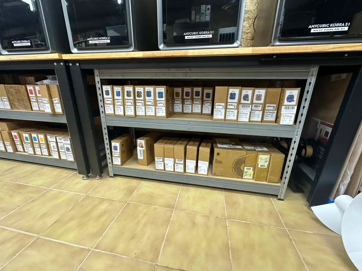 Racks de filament sous les machines, bobines rangées en boîtes étiquetées par matière et par teinte