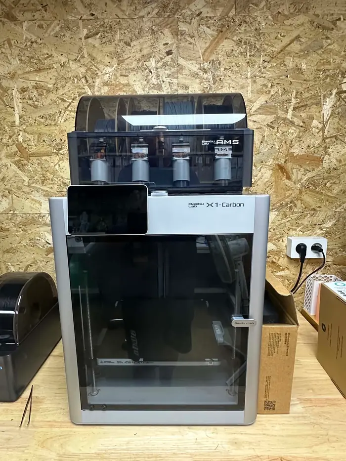 Imprimante Bambu Lab X1-Carbon surmontée de son chargeur AMS quatre bobines, posée sur l'établi