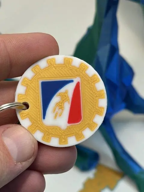 Porte-clés tenu à la main, blason bleu blanc rouge cerclé d'un engrenage jaune, imprimé en quatre couleurs