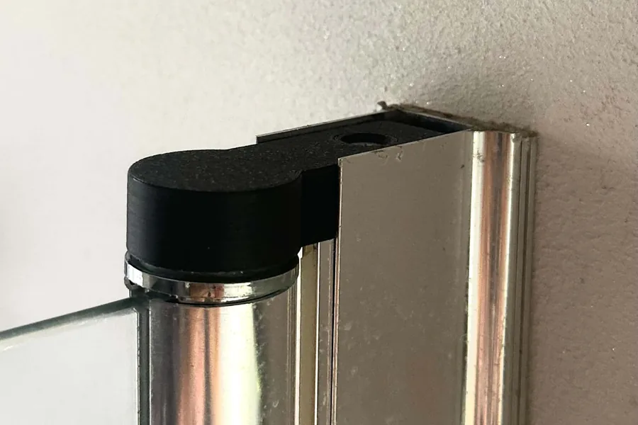 La butée noire imprimée en 3D, montée en haut du rail chromé d'une paroi de douche