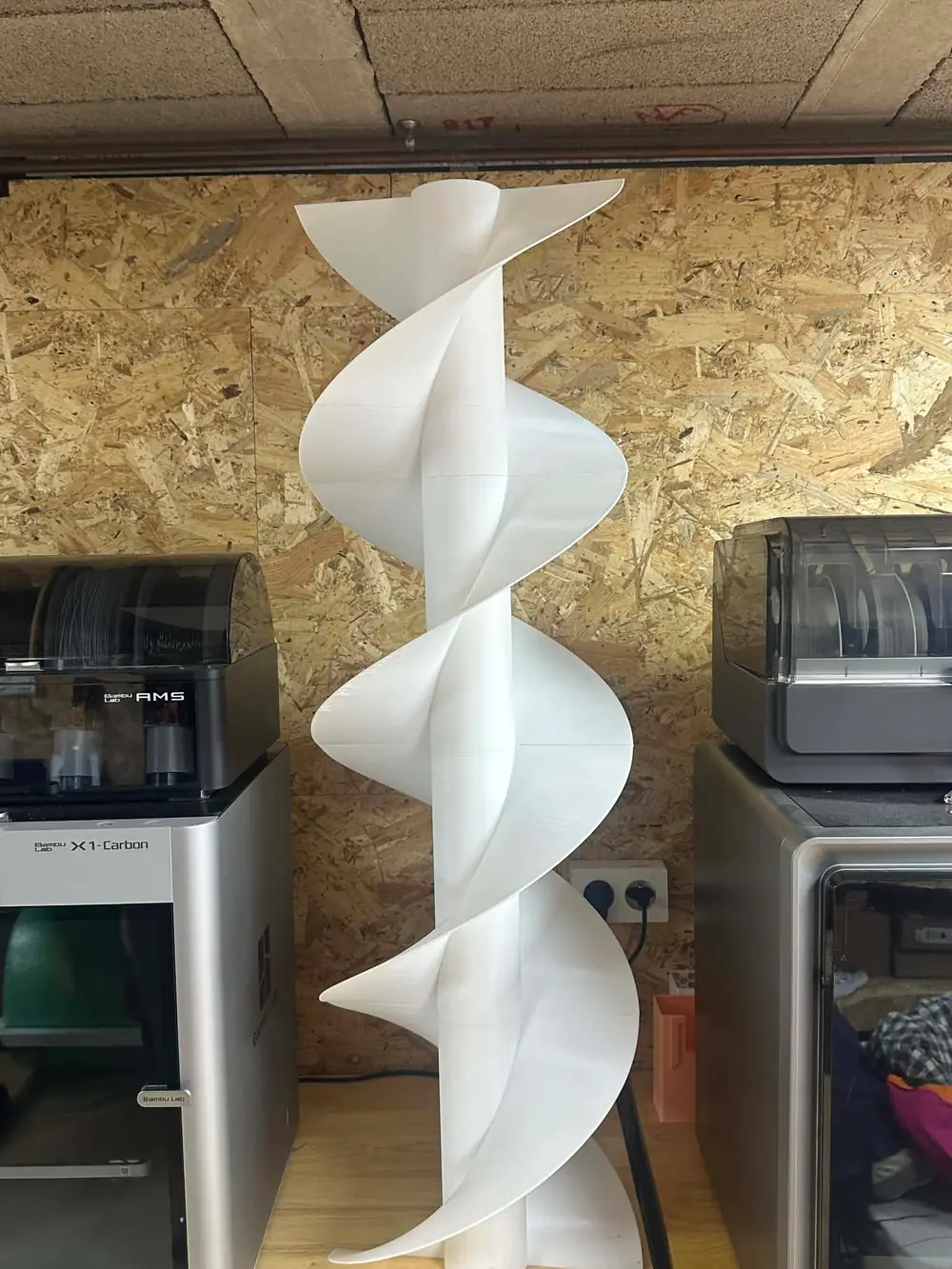 Grande vis sans fin blanche imprimée en 3D, dressée devant les imprimantes de l'atelier